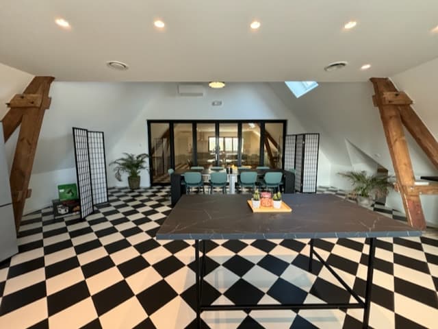 Intérieur d'un espace de travail moderne avec un sol en damier, des tables et des chaises, et des poutres en bois apparentes.