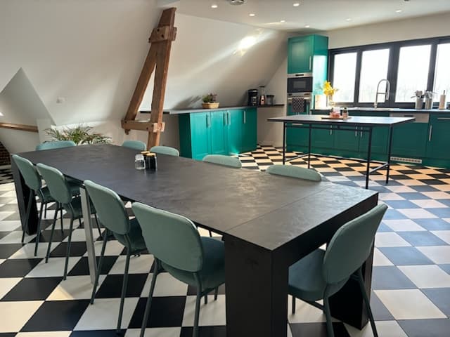 Une cuisine moderne avec un grand table noire entourée de chaises vertes, des armoires turquoise et un sol en damier noir et blanc.